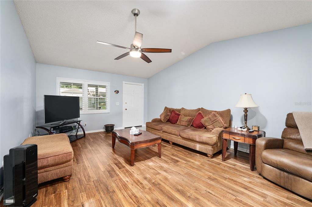 A living room features wood-look flooring, a ceiling fan, a sofa, and a television — 9820 SW 89TH TERRACE UNIT E, OCALA, FL