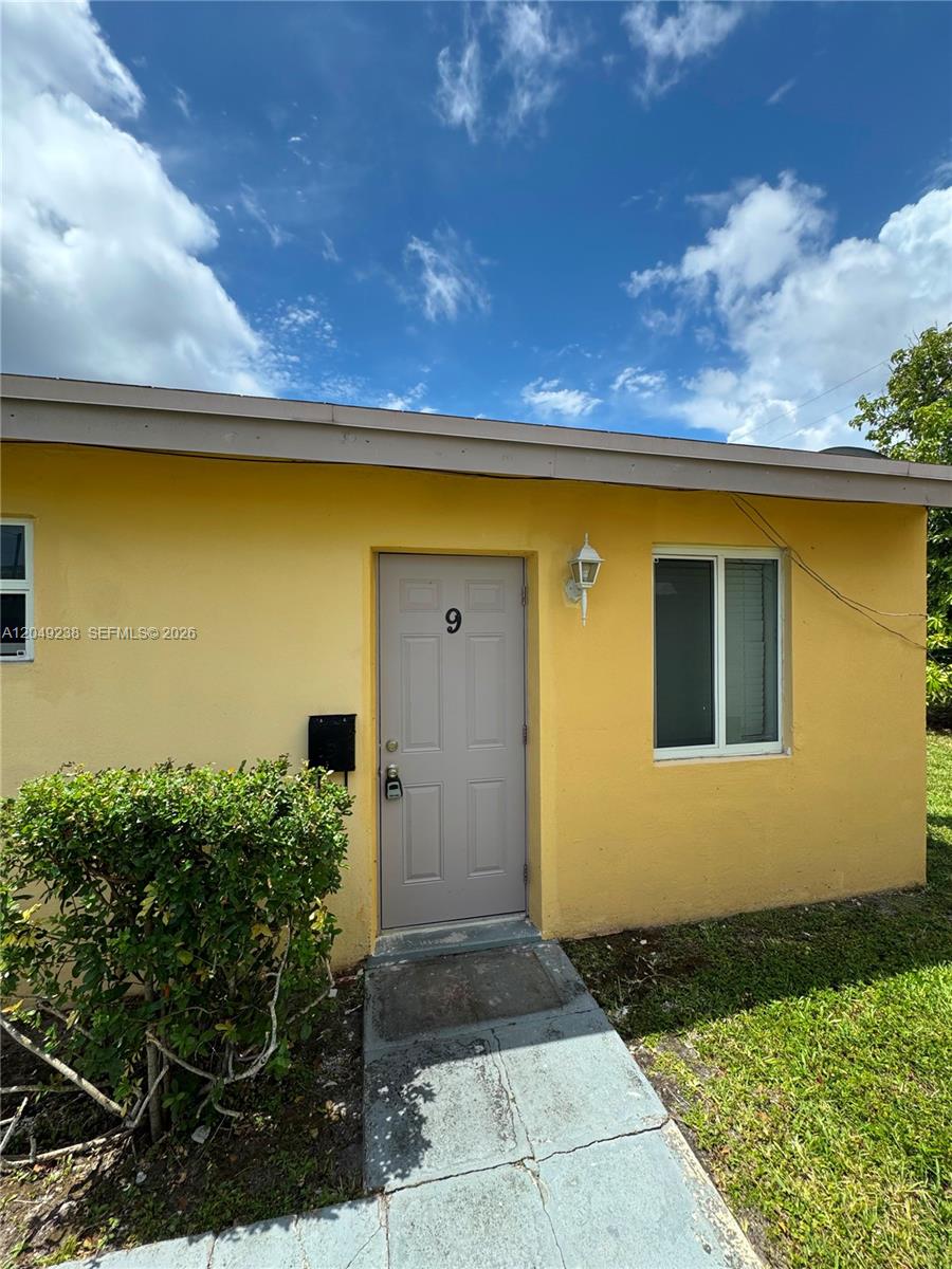 A yellow exterior wall features a gray front door labeled with the number nine — NORTH MIAMI BEACH, FL