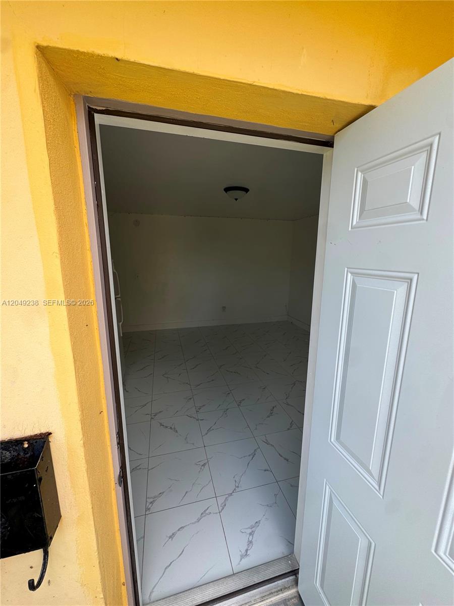 A white door opens into a small, empty room with white marble-patterned tile flooring — NORTH MIAMI BEACH, FL