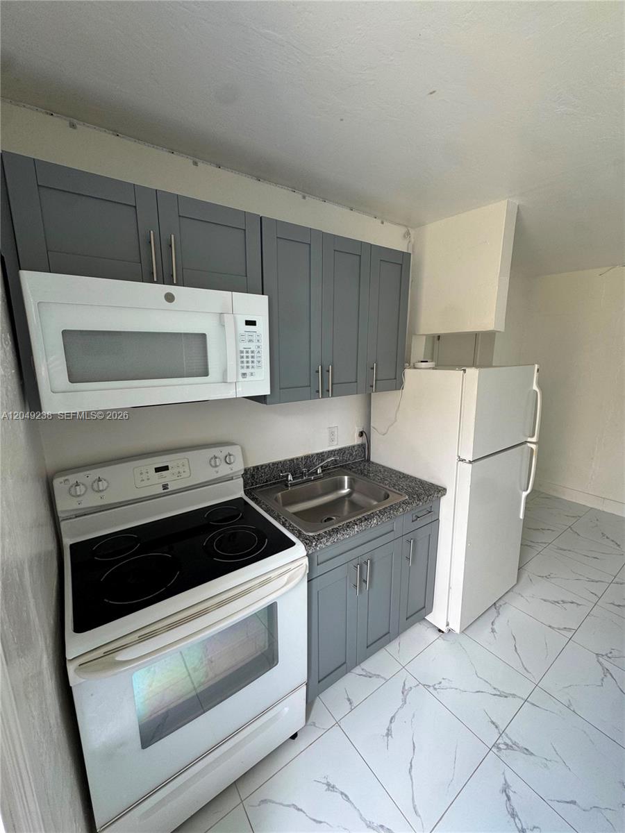 A small kitchen features gray cabinets, white appliances, a granite countertop, and white tiled floors — NORTH MIAMI BEACH, FL
