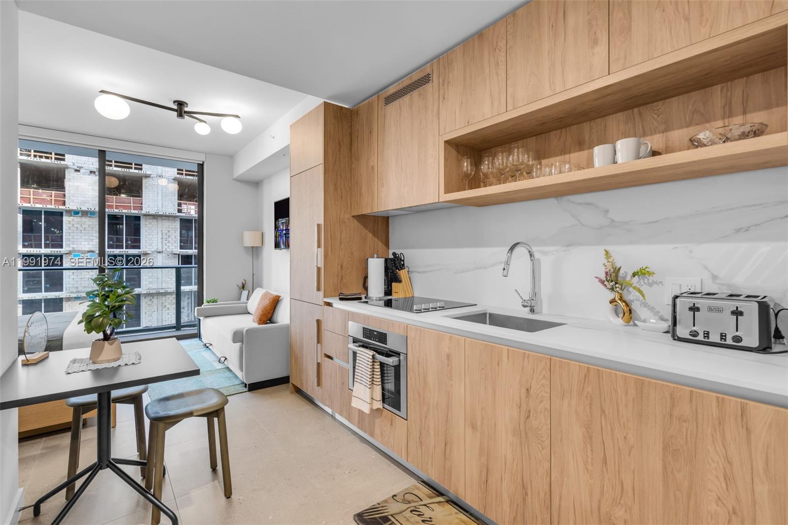 A modern kitchen features light wood cabinetry, white marble countertops, and an adjacent living area — 11 NE 6 th # 2808, Miami FL 33132, MIAMI, FL