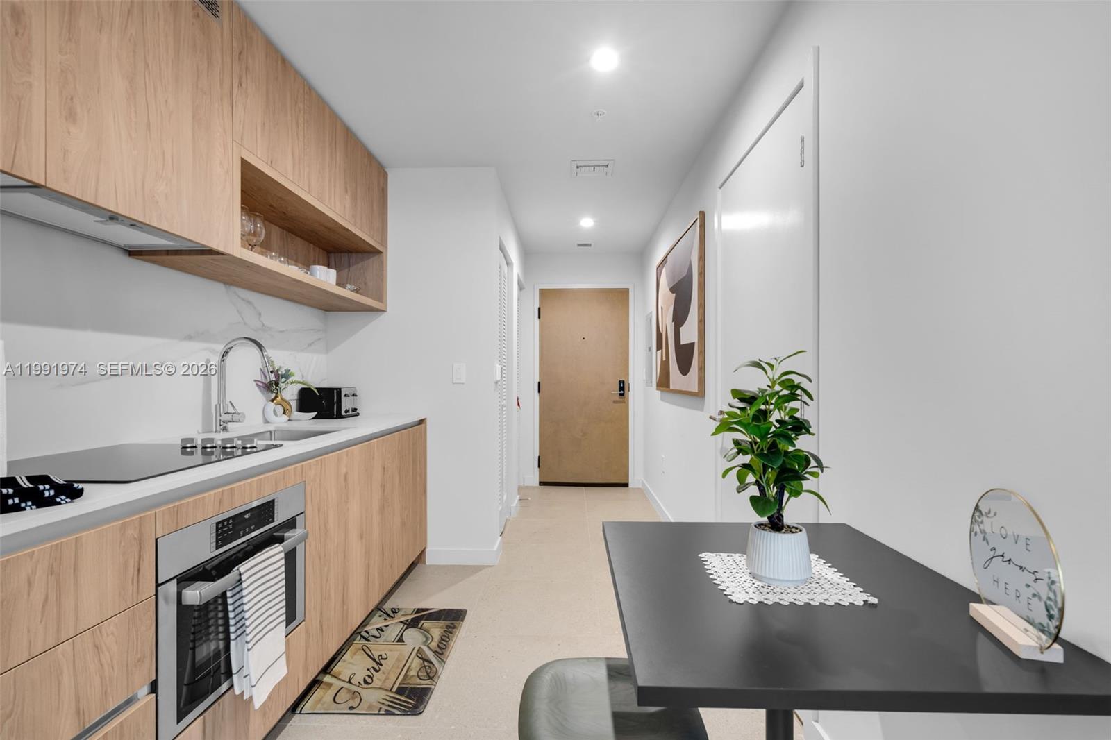 A modern kitchen features light wood cabinetry, white countertops, and a small dining table — 11 NE 6 th # 2808, Miami FL 33132, MIAMI, FL