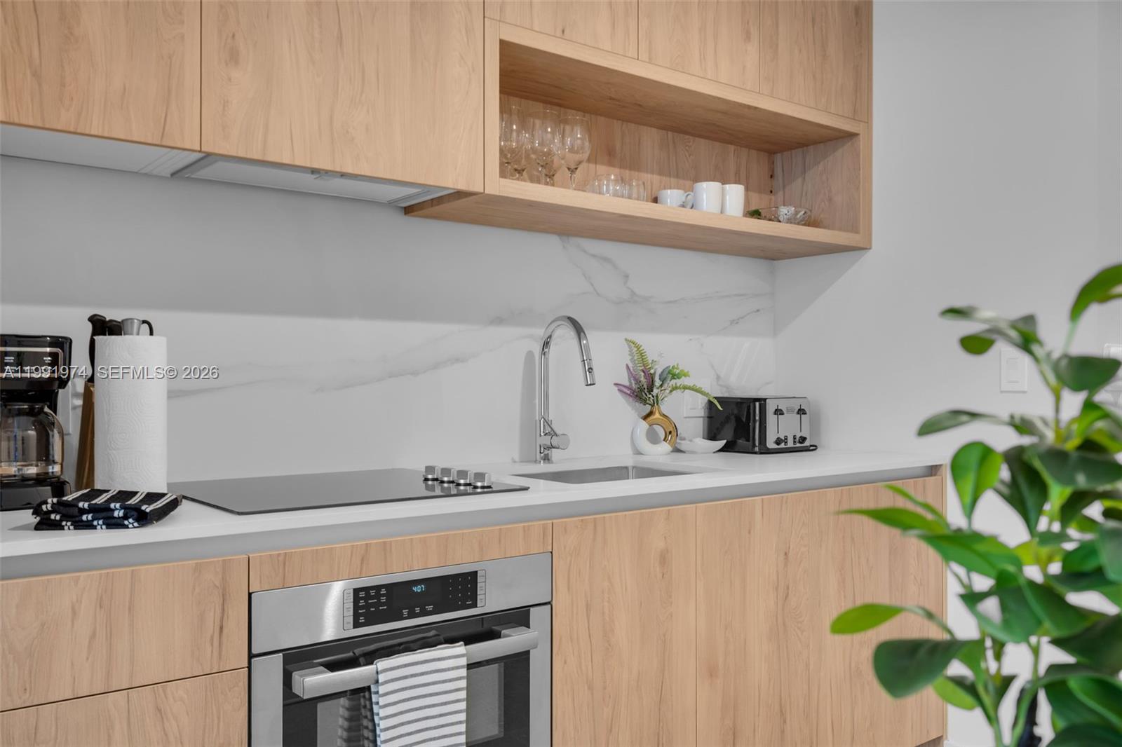 A modern kitchen features light wood cabinets, a marble backsplash, and stainless steel appliances — 11 NE 6 th # 2808, Miami FL 33132, MIAMI, FL