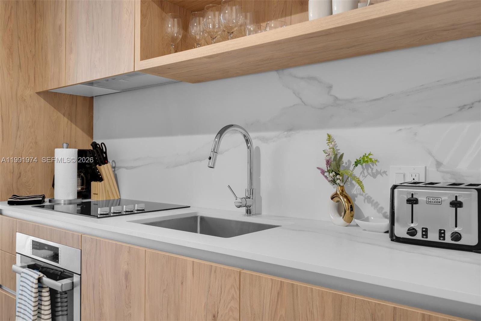 A modern kitchen features light wood cabinets, a white marble backsplash, and stainless steel appliances — 11 NE 6 th # 2808, Miami FL 33132, MIAMI, FL