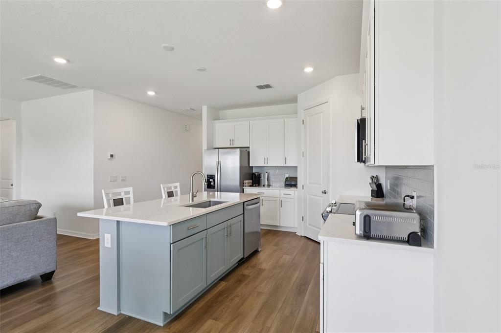 A kitchen features white cabinets, a light blue island with a sink, and wood-look flooring — 2326 GOLD DUST DRIVE, MINNEOLA, FL