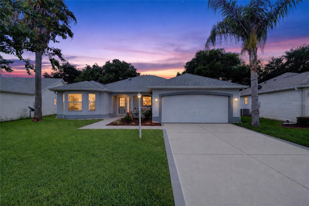 A single-story house with a two-car garage, a concrete driveway, and palm trees at dusk — 1832 MADERO DRIVE, LADY LAKE, FL