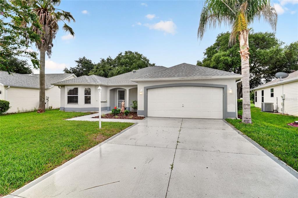 A single-story house with a white garage, gray roof, and a palm tree in front — 1832 MADERO DRIVE, LADY LAKE, FL