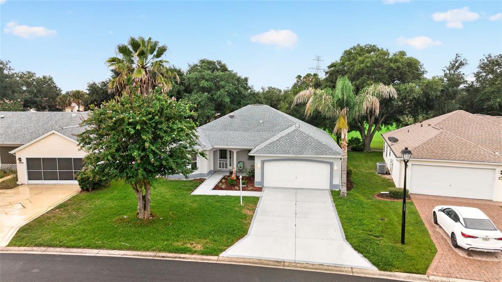 A single-story suburban house with a two-car garage, a concrete driveway, and mature landscaping — 1832 MADERO DRIVE, LADY LAKE, FL