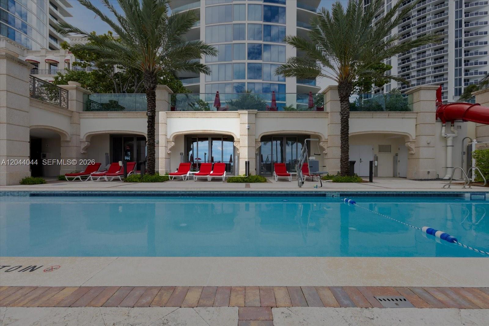 A swimming pool sits in front of a building with cabanas and lounge chairs — 17975 Collins Ave, Sunny Isles Beach FL 33160, SUNNY ISLES BEACH, FL