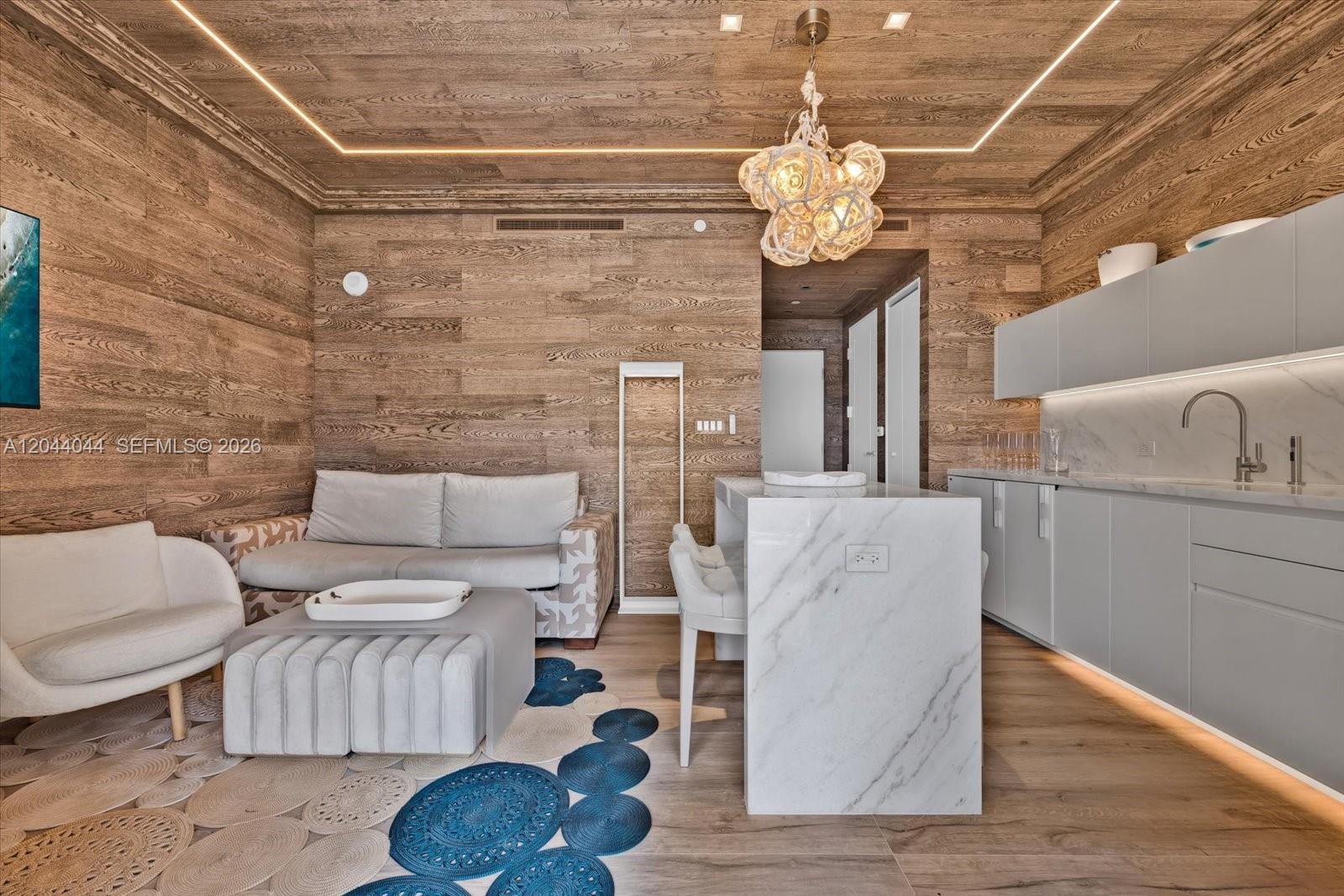 A modern living room and kitchen area features wood-paneled walls, a marble island, and lighting — 17975 Collins Ave, Sunny Isles Beach FL 33160, SUNNY ISLES BEACH, FL