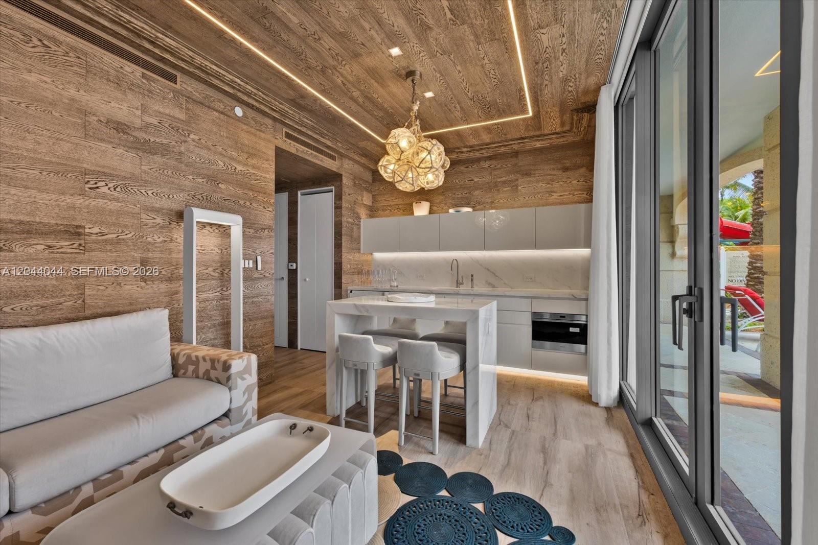 A modern kitchenette and living area feature wood-paneled walls, marble surfaces, and floor-to-ceiling windows — 17975 Collins Ave, Sunny Isles Beach FL 33160, SUNNY ISLES BEACH, FL