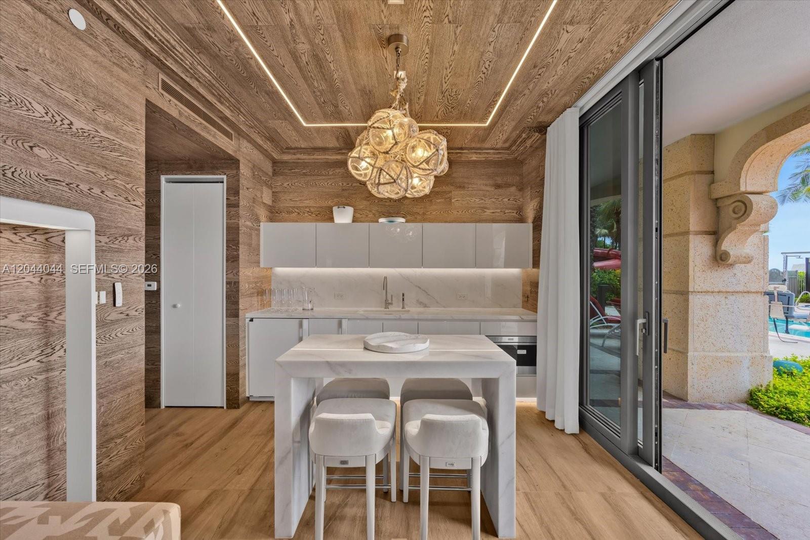A modern kitchen with wood-paneled walls and ceiling, marble island, and sliding glass patio doors — 17975 Collins Ave, Sunny Isles Beach FL 33160, SUNNY ISLES BEACH, FL