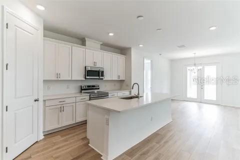A modern kitchen features white cabinetry, a central island, and light wood flooring — 453 ARCHWAY PLACE, ST CLOUD, FL
