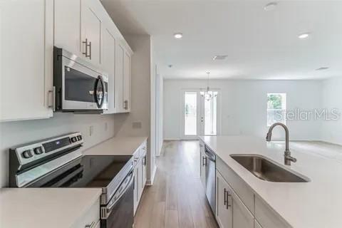 A modern kitchen features white cabinets, stainless steel appliances, and an island with a sink — 453 ARCHWAY PLACE, ST CLOUD, FL