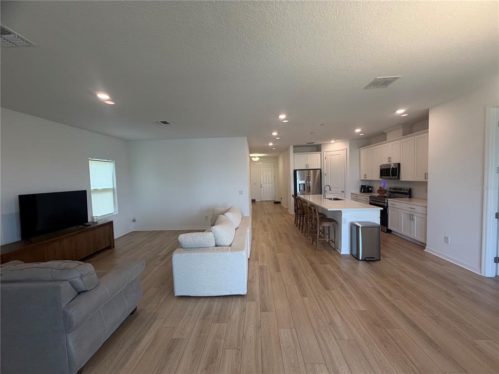 An open-concept living room and kitchen with white cabinets, light wood floors, and recessed lighting — 453 ARCHWAY PLACE, ST CLOUD, FL