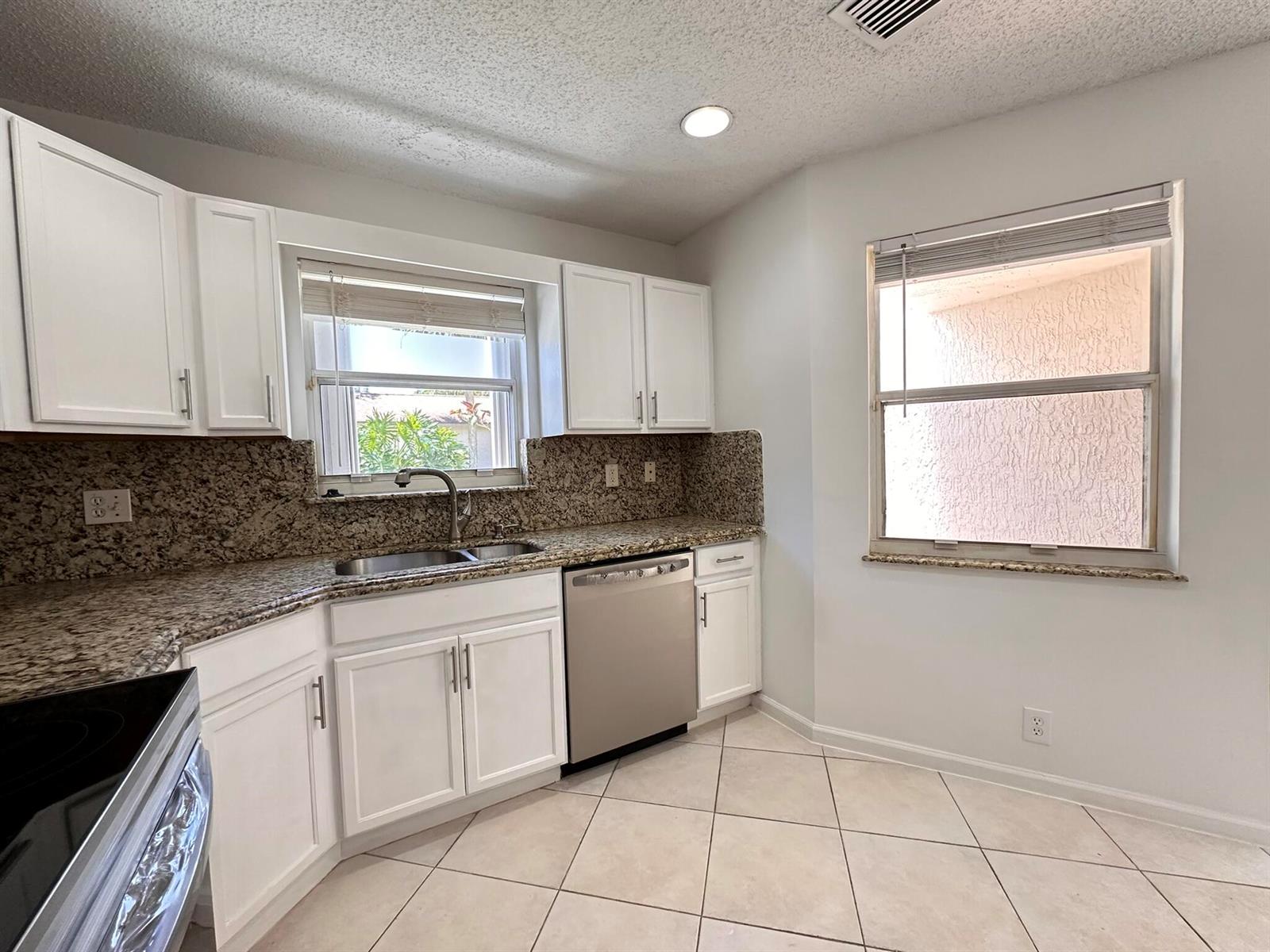 A kitchen with white cabinets, granite countertops, stainless steel appliances, and light-colored tile flooring — 703 Crosswinds Drive, FL 33413, FL