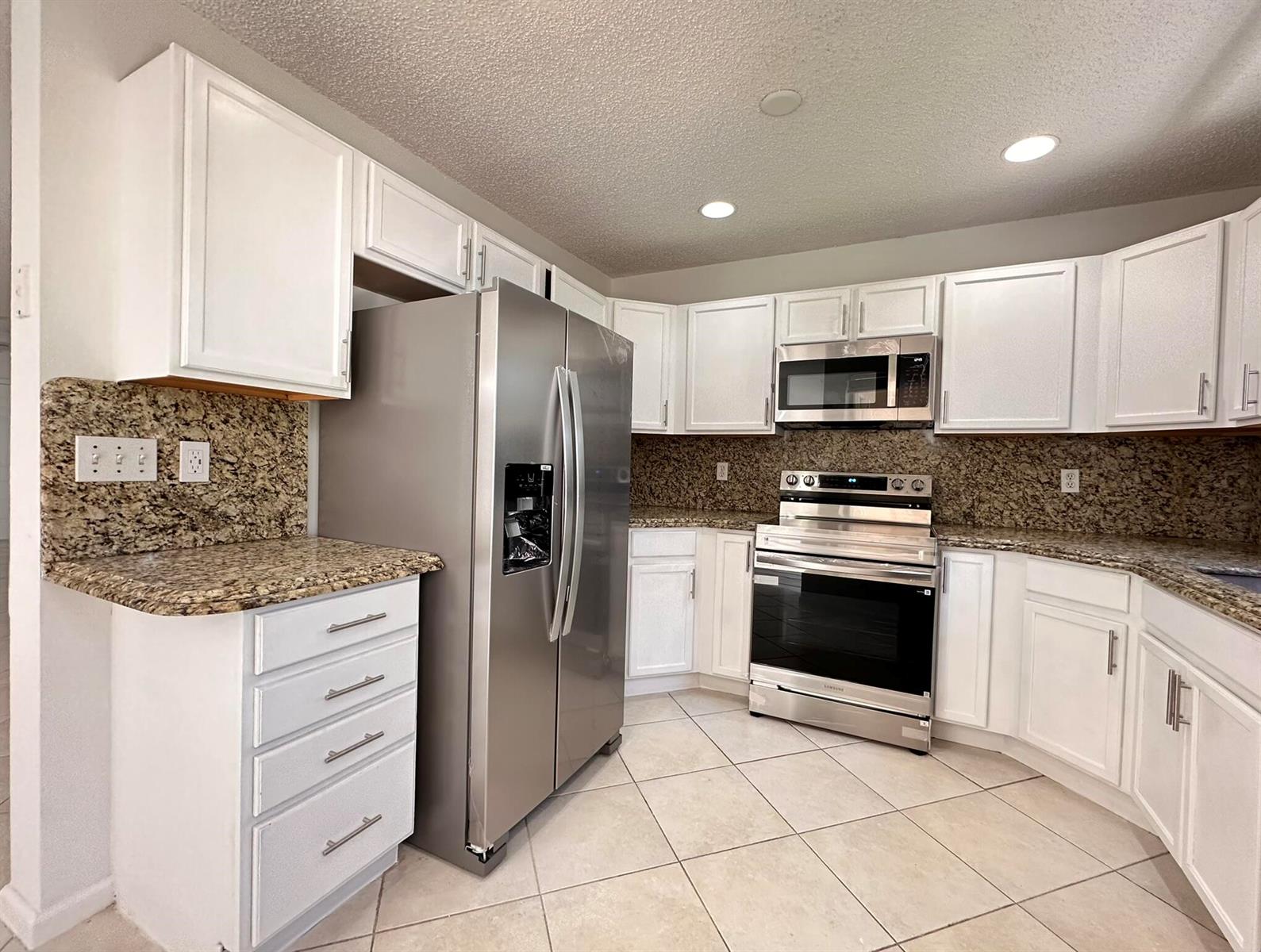 A kitchen features white cabinets, stainless steel appliances, and speckled granite countertops — 703 Crosswinds Drive, FL 33413, FL