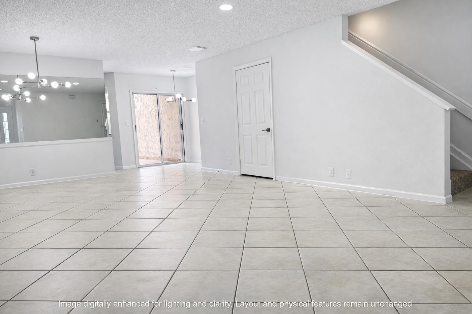 An empty room with light-colored tile flooring, white walls, a staircase, and a sliding glass door — 703 Crosswinds Drive, FL 33413, FL
