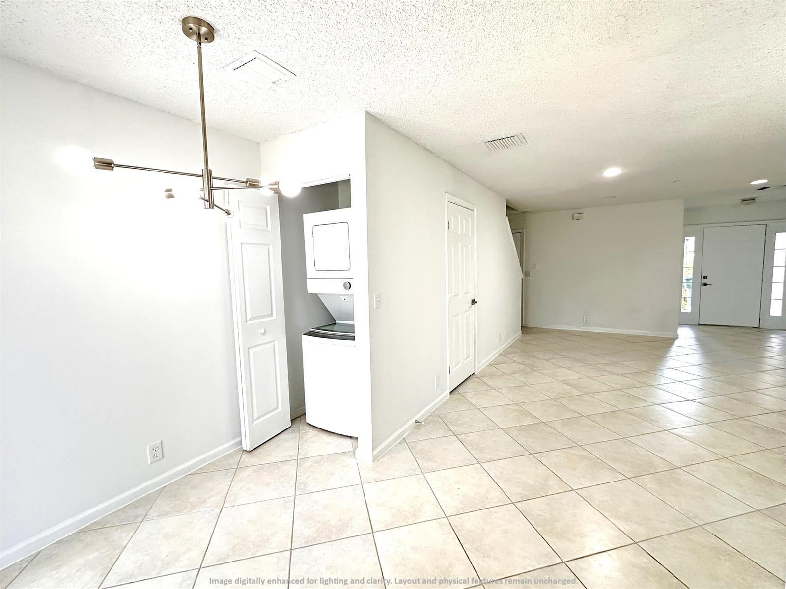 A room with tiled floors, a stacked washer-dryer unit, and a modern light fixture — 703 Crosswinds Drive, FL 33413, FL