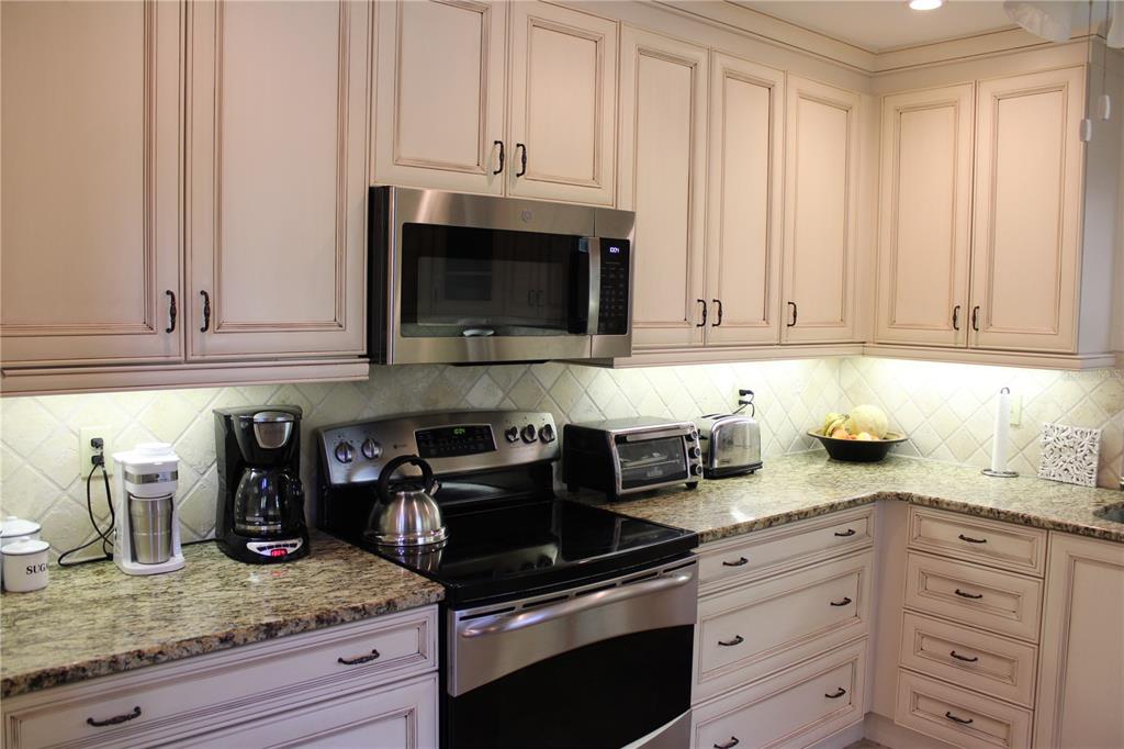 A kitchen features cream-colored cabinets, granite countertops, stainless steel appliances, and a tiled backsplash — 7909 4TH AVENUE W UNIT 12, BRADENTON, FL