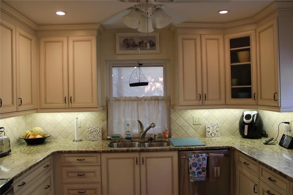 A kitchen features cream-colored cabinets, granite countertops, a double sink, and a window with decor — 7909 4TH AVENUE W UNIT 12, BRADENTON, FL