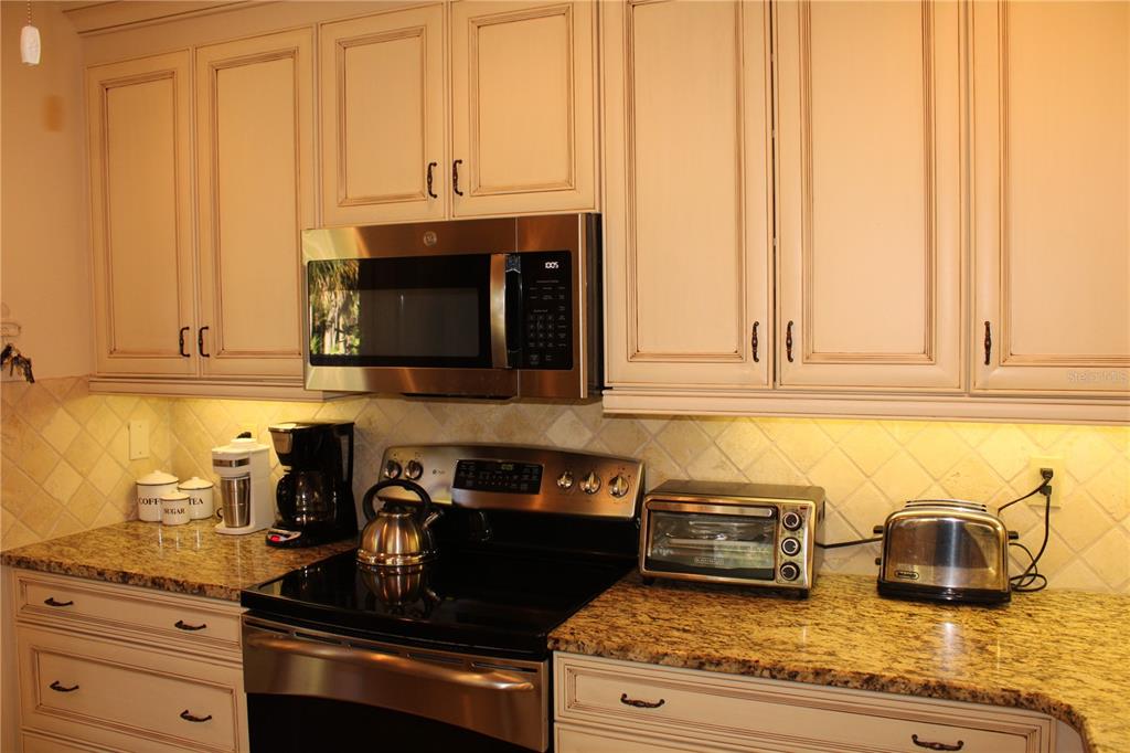 A kitchen features cream-colored cabinets, granite countertops, stainless steel appliances, and a tiled backsplash — 7909 4TH AVENUE W UNIT 12, BRADENTON, FL