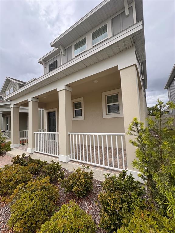 A two-story house features a covered front porch with white railings and beige stucco siding — 1563 CROSS PRAIRIE PARKWAY, KISSIMMEE, FL