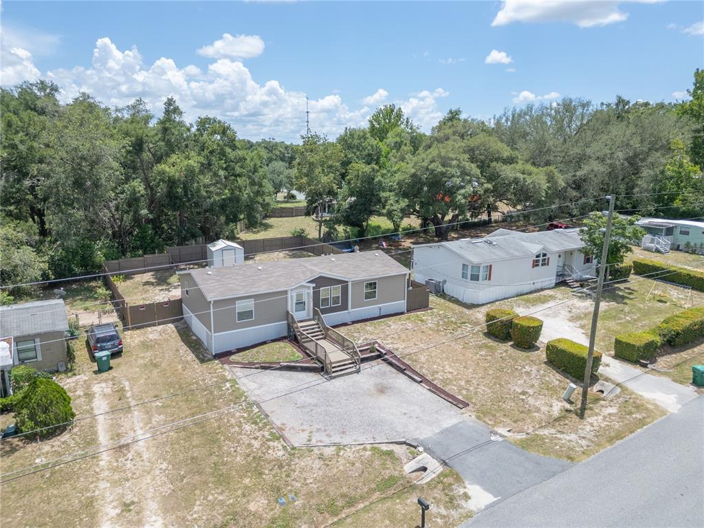 An aerial view shows a tan manufactured home with a gravel driveway and wooden steps — 242 SKYLINE DRIVE, LADY LAKE, FL