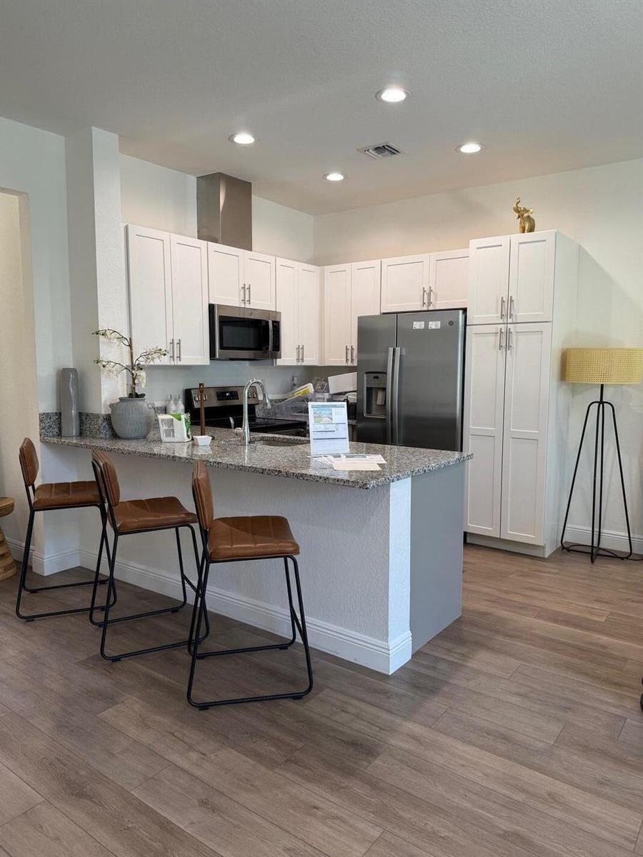 A kitchen features white cabinets, granite countertops, stainless steel appliances, and three brown bar stools — 341 Oak Alley, Delray Beach FL 33444, DELRAY BEACH, FL