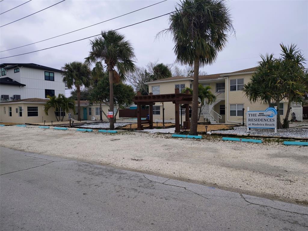 An exterior view of a two-story apartment building with palm trees and a wooden pergola — 115 145TH AVENUE E UNIT 3, MADEIRA BEACH, FL