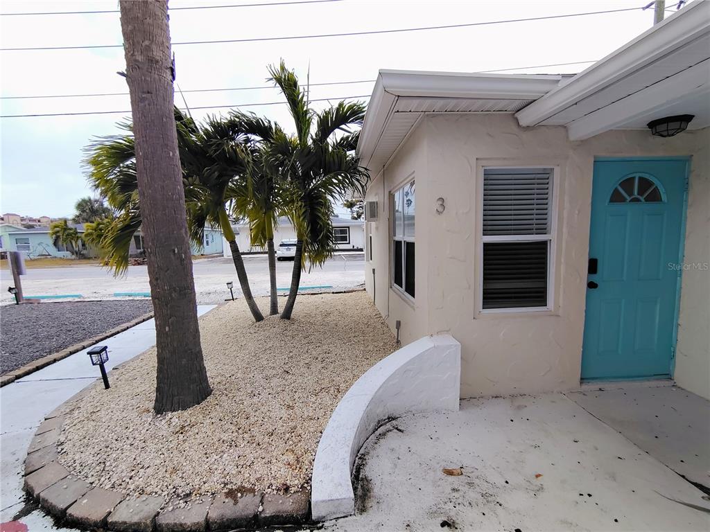 The exterior of a beige building features a turquoise door and a gravel landscaping bed — 115 145TH AVENUE E UNIT 3, MADEIRA BEACH, FL