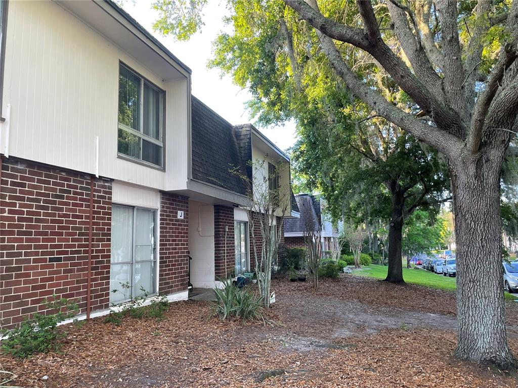 A two-story brick and siding townhouse exterior with a large tree in the front yard — 1700 SW 16TH COURT UNIT J24, GAINESVILLE, FL