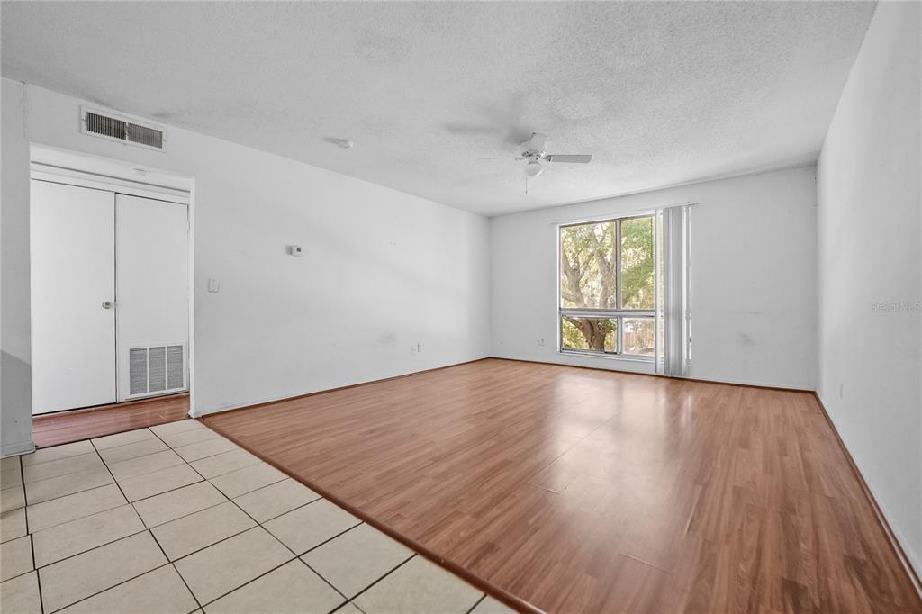 An empty living room features wood-look flooring, white walls, a ceiling fan, and a window — 1700 SW 16TH COURT UNIT J24, GAINESVILLE, FL