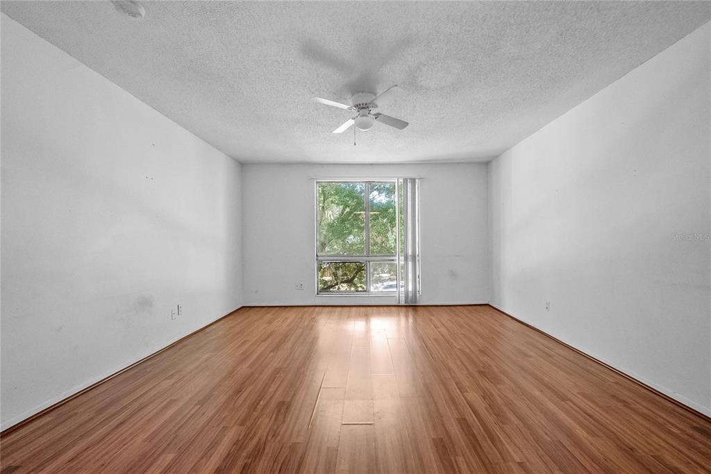 An empty room with wood-look flooring, white walls, a ceiling fan, and a large window — 1700 SW 16TH COURT UNIT J24, GAINESVILLE, FL