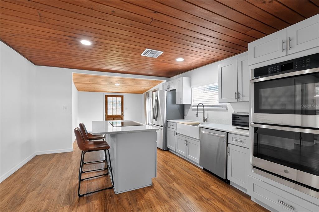 A kitchen features light gray cabinetry, a central island, and a wood-paneled ceiling — 4746 LAMAR ROAD, ZEPHYRHILLS, FL