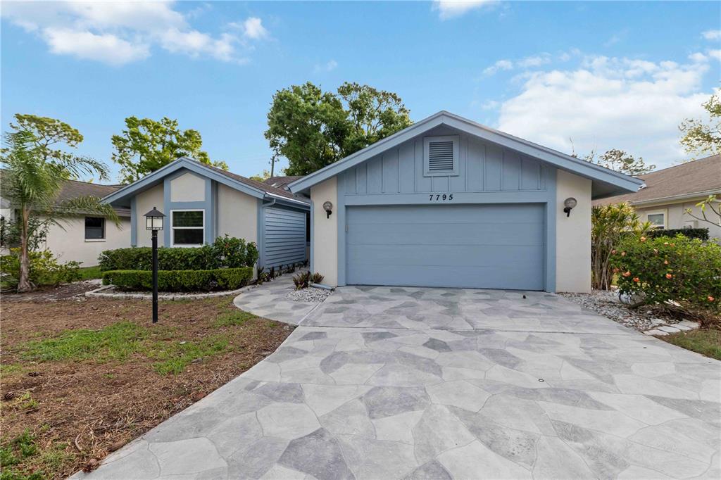 A single-story house with a blue garage door and a patterned concrete driveway — 7795 PINE TRACE, SARASOTA, FL