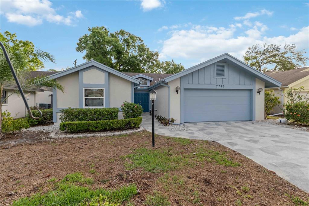 A single-story house with a blue-trimmed exterior, a two-car garage, and a paved driveway — 7795 PINE TRACE, SARASOTA, FL