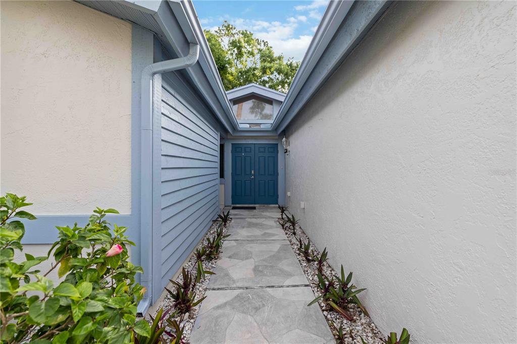 A stone walkway leads to a blue double-door entrance between two exterior walls — 7795 PINE TRACE, SARASOTA, FL