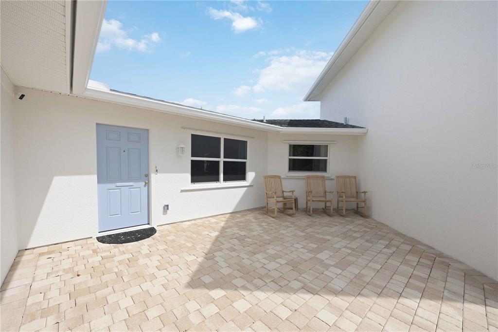 A paved courtyard features a light blue door, three wooden rocking chairs, and white walls — 917 CHURCH STREET, VENICE, FL