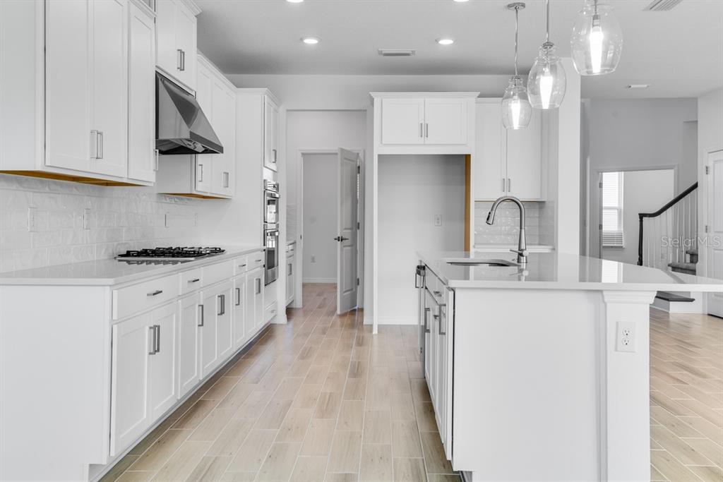 A modern kitchen features white cabinetry, a central island, stainless steel appliances, and light flooring — 846 JUNONIA BOULEVARD, NEW SMYRNA BEACH, FL