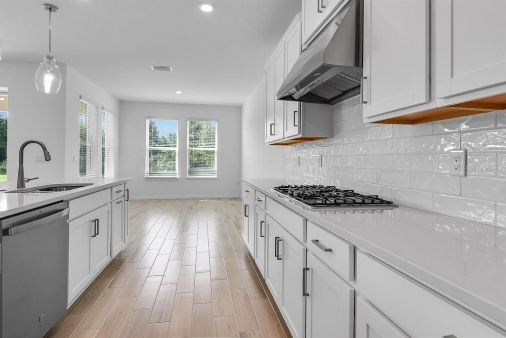 A modern white kitchen features a large island, stainless steel appliances, and light wood-look flooring — 846 JUNONIA BOULEVARD, NEW SMYRNA BEACH, FL