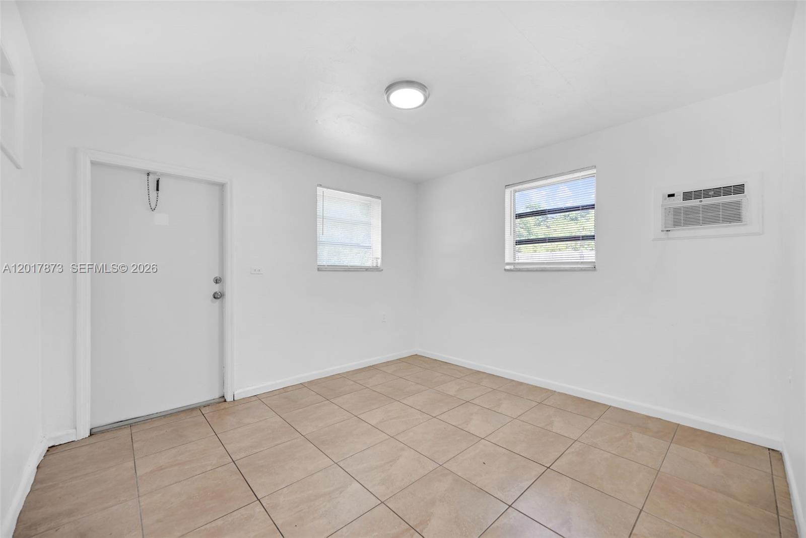 A sparsely furnished room features white walls, tiled floors, two windows, and a wall-mounted air conditioner — 567-3 NW 90th St, El Portal FL 33150, EL PORTAL, FL
