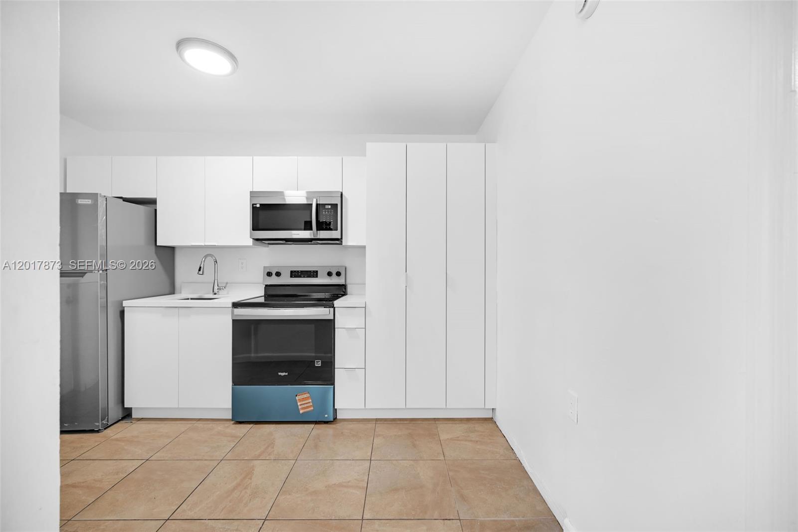 A kitchen features white flat-panel cabinets, stainless steel appliances, and light-colored tile flooring — 567-3 NW 90th St, El Portal FL 33150, EL PORTAL, FL