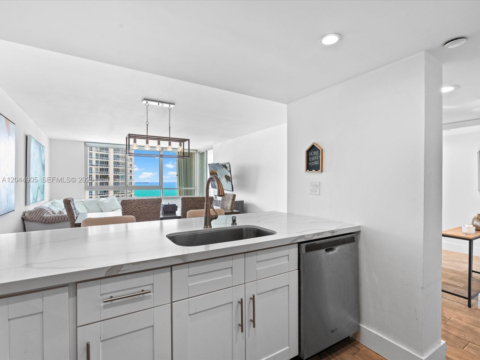 A kitchen with white cabinets and a stainless steel dishwasher overlooks a living area — 400 S Pointe Dr # 1102, Miami Beach FL 33139, MIAMI BEACH, FL