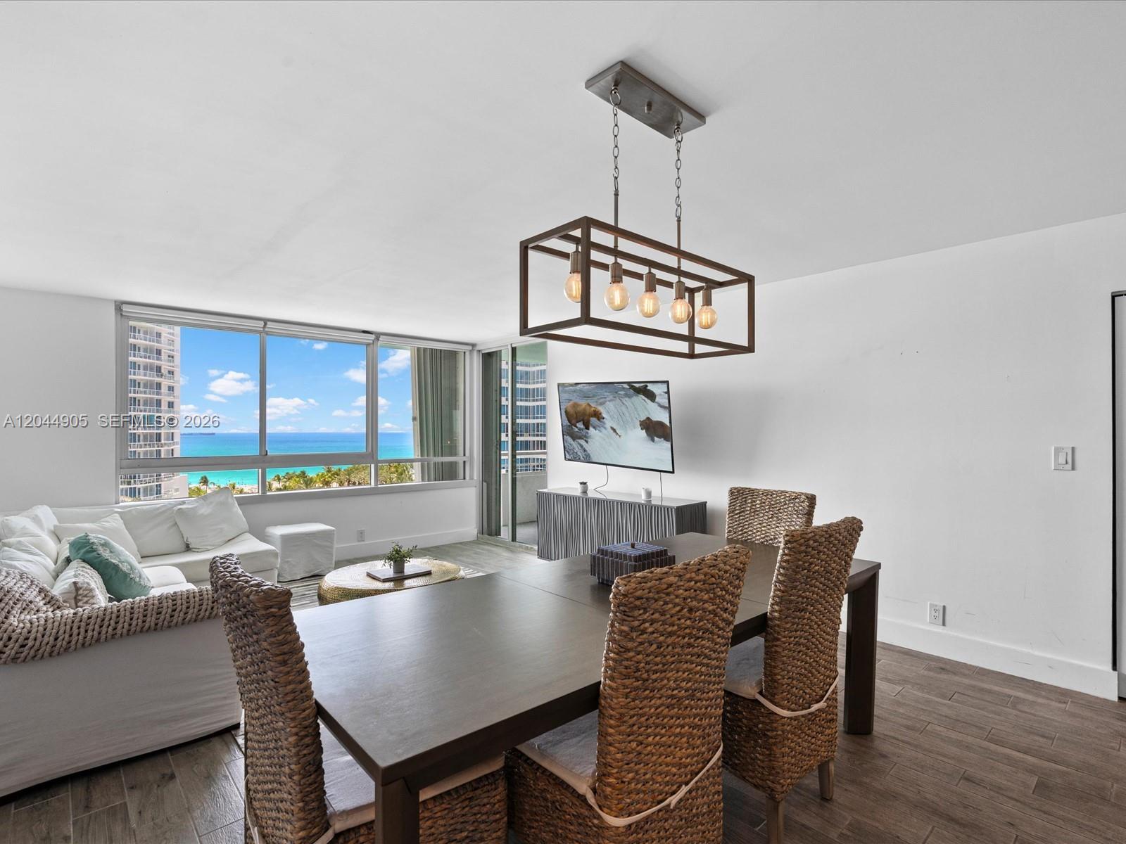 A dining area with a wooden table and wicker chairs sits before a coastal view — 400 S Pointe Dr # 1102, Miami Beach FL 33139, MIAMI BEACH, FL