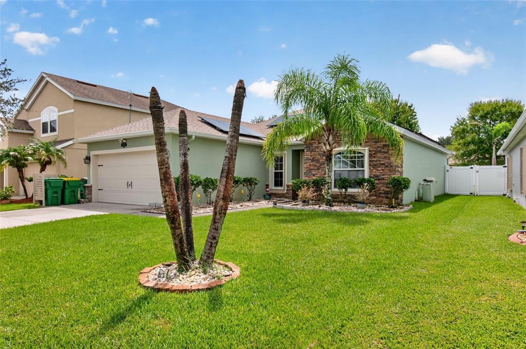 A single-story house with a light green exterior, stone accents, a palm tree, and garage — 1465 LITCHFIELD DRIVE, WEST MELBOURNE, FL