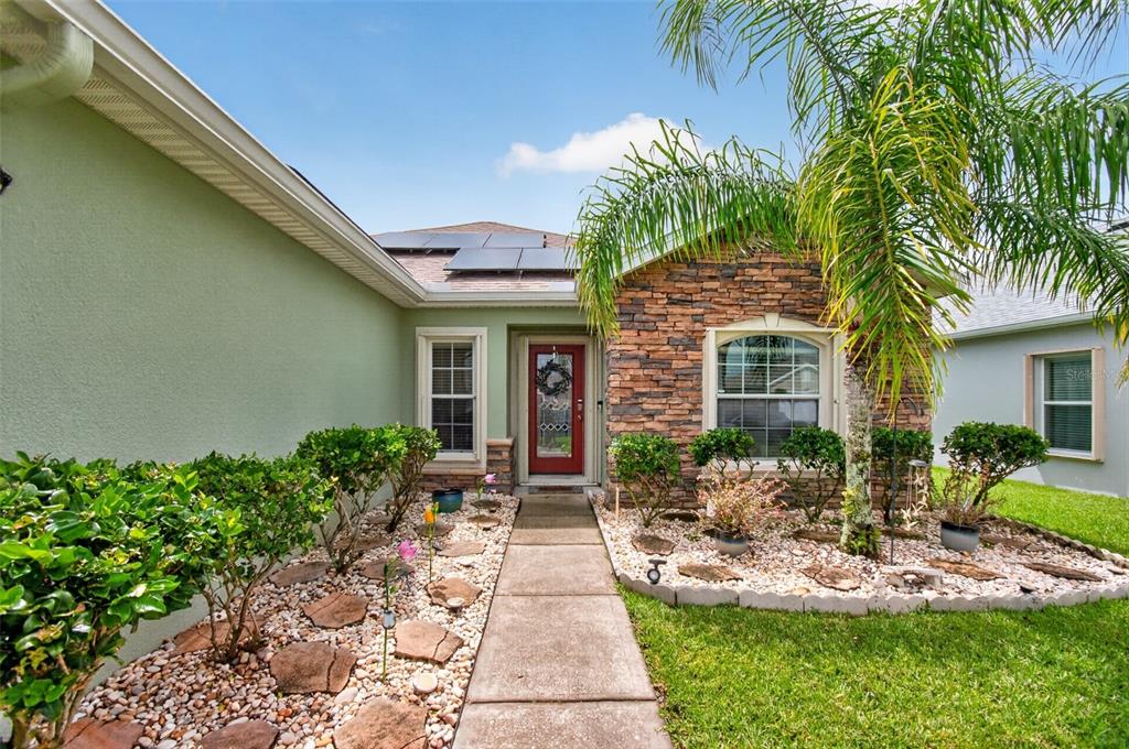 A front exterior view of a house with a stone facade, red door, and landscaping — 1465 LITCHFIELD DRIVE, WEST MELBOURNE, FL
