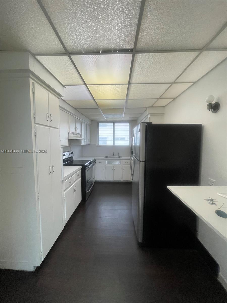 A galley-style kitchen features white cabinets, dark flooring, and a drop ceiling with lights — 10178 Collins Ave # 202, Bal Harbour FL 33154, BAL HARBOUR, FL
