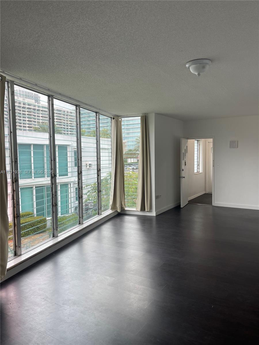 An empty room features dark flooring, white walls, and floor-to-ceiling windows overlooking a building — 10178 Collins Ave # 202, Bal Harbour FL 33154, BAL HARBOUR, FL