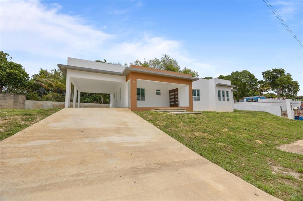 A modern, single-story house with a concrete driveway, a carport, and a brown-accented entrance — solar 2 villa alemeria MARCEL, AGUADILLA, PR